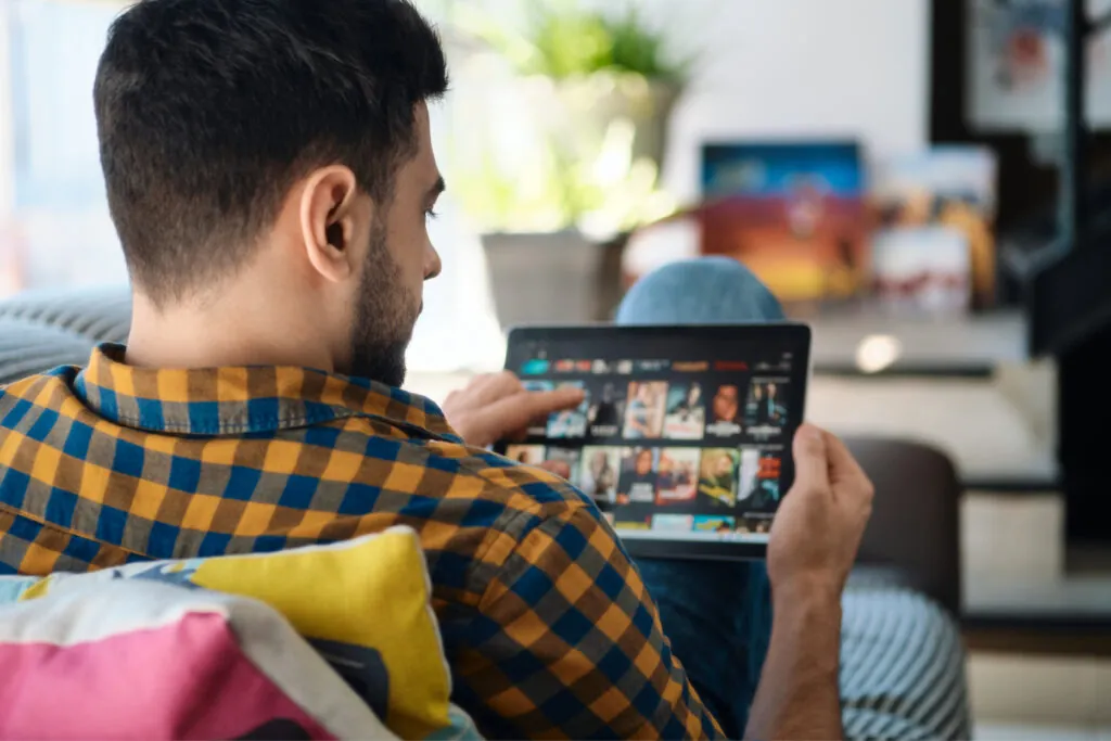 Man streaming content on a tablet at home, representing the OTT experience in the context of OTT vs CTV.