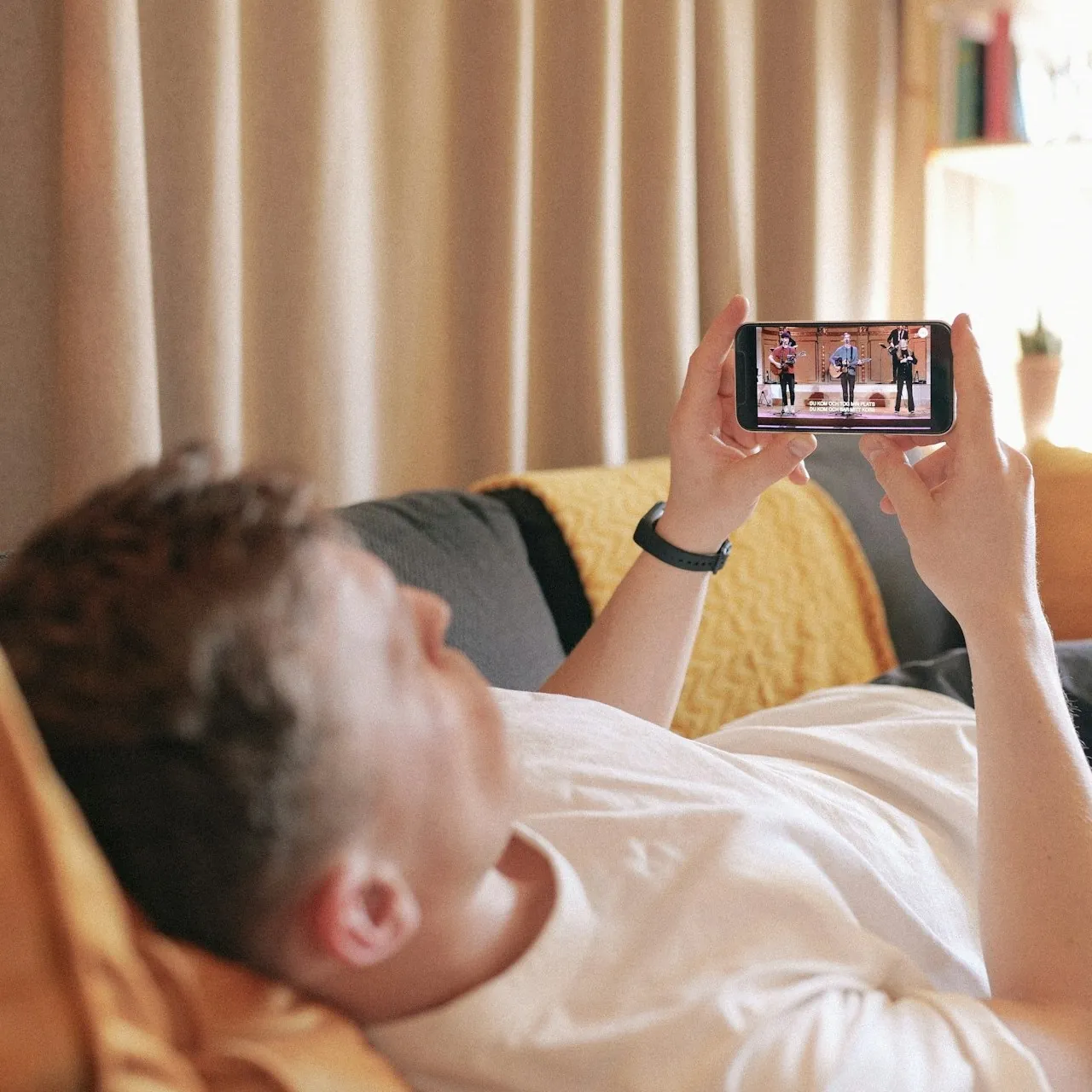 Student watching video on smartphone while relaxing on couch, showing benefits of TV advertising on streaming devices